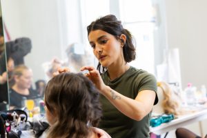 A lady standing up doing another lady's hair who is sitting down