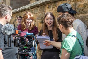 A group of 4 students chatting behind a camera.